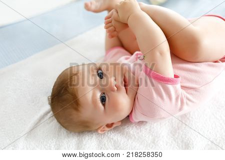 Cute baby taking feet in mouth. Adorable little baby girl sucking own foot.