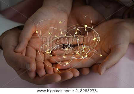 Christmas garland in the hands of a couple. A man and a woman hold a light garland on the palms of their hands.