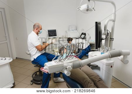 Process Of Preparing And Installing Dental Ceramic Crown. Male Professional Dentist And Female Assis