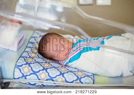 Sleeping baby boy resting in a hospital crib in a hospital delivery room. The ethnically diverse child is peaceful and content in his bed