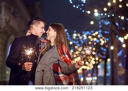 A young couple laughing with Bengal lights in the hands of a city street.