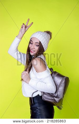 beautiful cheerful girl with a backpack in a sweater on a bright isolated background of yellow color
