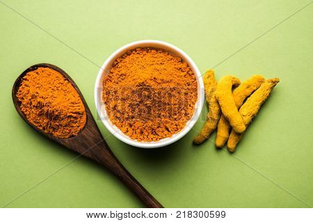 Turmeric powder in ceramic bowl with raw dried turmeric over plain background