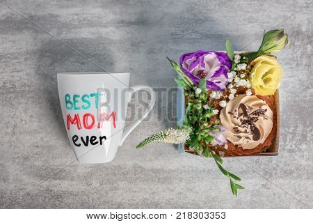Cup with text BEST MOM EVER, cake and flowers in gift box for Mother's day on grey background