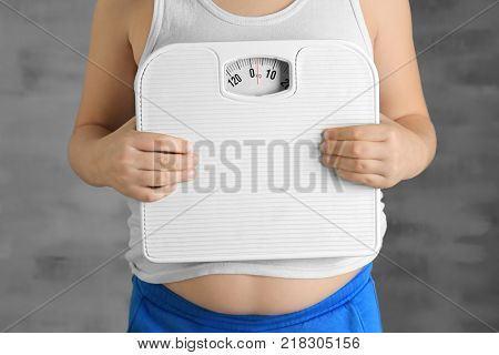 Overweight boy with scales on grey background, closeup