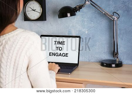 Laptop with text TIME TO ENGAGE on screen and woman at table
