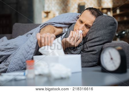 Running nose. Low-spirited male person wrinkling forehead and stretching hand while wiping nose
