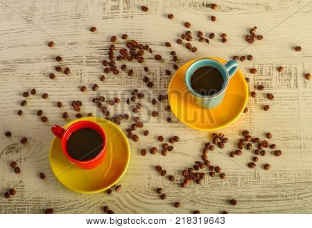 two coffee cups with diferent colors with coffee beans liyng in the background