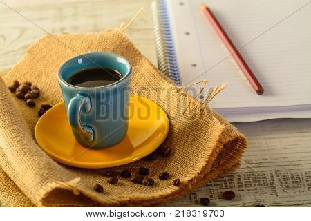 coffee cup with coffee beans liyng in the background with a book for taking notes on side