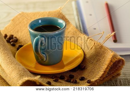 coffee cup with coffee beans liyng in the background with a book for taking notes on side