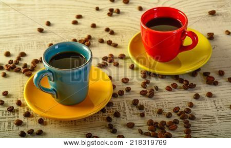 two coffee cups with diferent colors with coffee beans liyng in the background