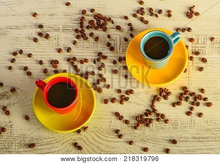 two coffee cups with diferent colors with coffee beans liyng in the background