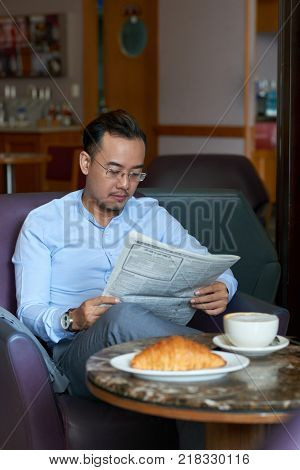 Handsome Asian businessman reading newspaper and drinking coffee in coffeshop