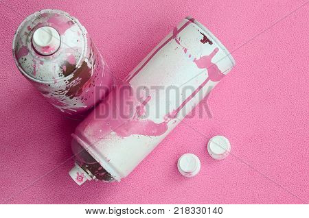 Some used pink aerosol spray cans and nozzles with paint drips lies on a blanket of soft and furry light pink fleece fabric. Classic female design color. Graffiti hooliganism concept