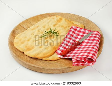 two pieces of traditional Tuscan flatbread (Ghiottina Toscana) and kitchen knife on round wooden cutting board