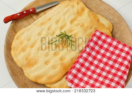 two pieces of traditional Tuscan flatbread (Ghiottina Toscana) and kitchen knife on round wooden cutting board - close up
