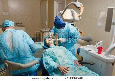Male Old Professional Dentist Surgeon In Uniform And Female Assistant Helps To Performing Operation