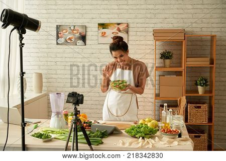 Pretty Vietnaemse female blogger showing bowl of salad she made to camera