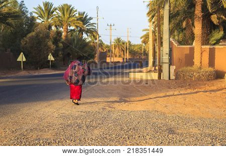 M'hamid Morocco - February 22 2016: Rear view of unidentified woman carrying jute burlap sack during evening