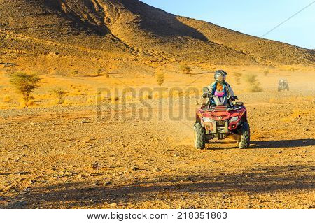 Ait Saoun Morocco - February 23 2016: Woman riding quad bike in the Ait Saoun desert of Morocco near mountains.