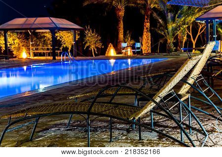 M'hamid Morocco - February 22 2016: Swimming-pool in resort with around deck-chairs for relaxing in blue sea water night scene. M'Hamid El Ghizlane is a small oasis town in southern Morocco.