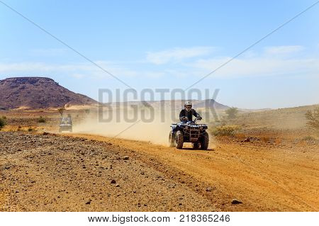 Young man in bike dress and helmet riding quad bike in desert