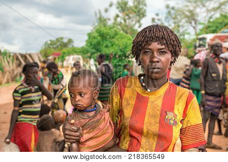 TURMI, OMO VALLEY, ETHIOPIA - MAY 5, 2015: Portrait of a woman from the Hamar tribe with her baby in south Ethiopia. Married hamar women apply red clay to their hair and fashion it into long tufts.