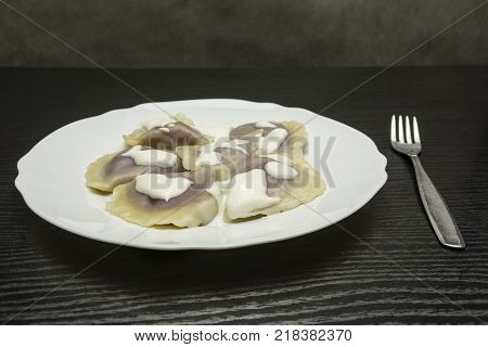 Plate of boiled dumplings with cottage quark and blueberry filling topped with cream on a wooden dark table.