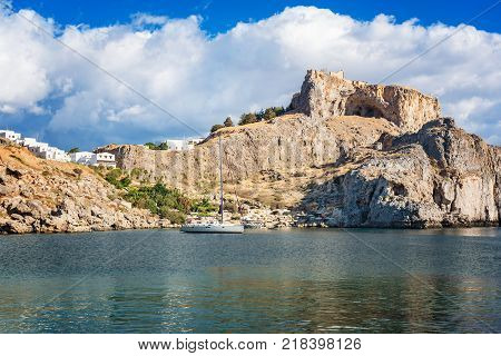 Sail boat in St. Paul´s bay cloudy blue sky Lindos acropolis in background (Rhodes Greece)