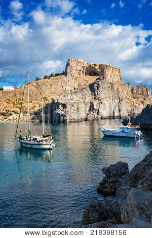 Sail boats in St. Paul´s bay cloudy blue sky Lindos acropolis in background (Rhodes Greece)