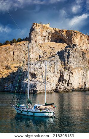 Sail boat in St. Paul´s bay cloudy blue sky Lindos acropolis in background (Rhodes Greece)