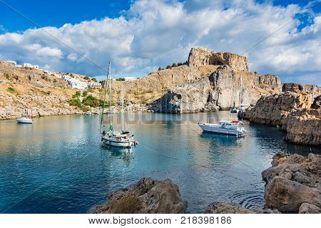 Sail boats in St. Paul´s bay cloudy blue sky Lindos acropolis in background (Rhodes Greece)
