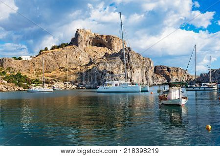 Fishing boats and sail boat in St. Paul´s bay Lindos acropolis in background (Rhodes Greece)