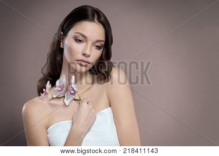 Young and healthy woman with light make-up is holding the Orchid flower. Beige background. SPA and skin care concept.
