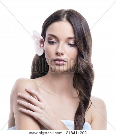 Young and healthy woman with light make-up on white background. The hair is decorated with beautiful fresh Orchid flower. SPA and skin care concept.