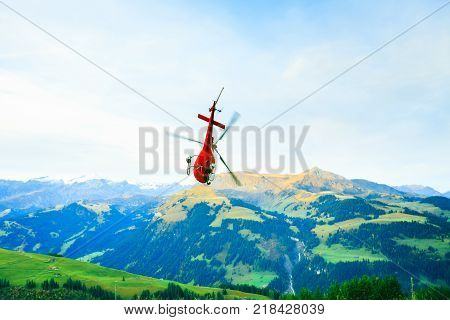 red helicopter flying over the simmental valley in the swiss alps.