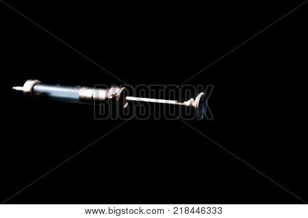 Old syringe without a needle isolated on black.