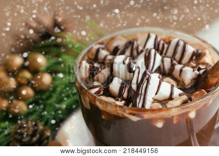 Hot chocolate in cup topping with marshmallow and chocolate sauce. Delicious hot chocolate or cacoa on wood table in close up view, copy space with Christmas theme and snowfall background. Concept to present Xmas drink. Homemade hot chocolate.