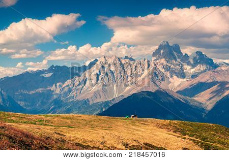 Colorful autumn landscape with shepherd house and green tourist tent. Sunny morning scene with mountain Ushba on the background. Mkheer Svaneti Georgia Europe. Artistic style post processed photo.