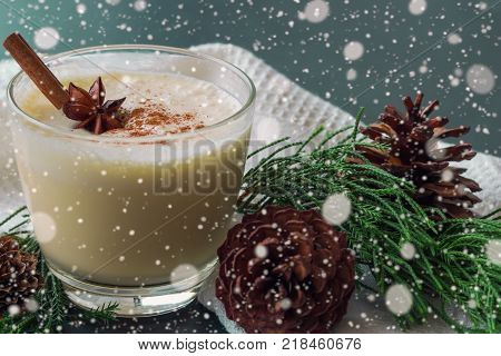 Eggnog traditional drink for Christmas celebration party. Homemade eggnog in glass topped with ground nutmeg and cinnamon stick. Eggnog in top view with copy space in Christmas theme decoration and snowfall background. Delicious eggnog ready to served.