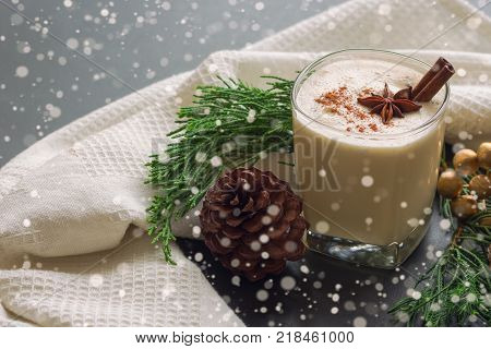 Eggnog traditional drink for Christmas celebration party. Delicious eggnog in glass topped with ground nutmeg and cinnamon stick. Eggnog in top view copy space in Christmas theme decoration and snowfall effect background. hommade eggnog ready to served.
