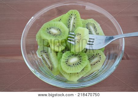 Bowl full with high in vitamins Kiwi fruit slices and fork isolated on wooden background