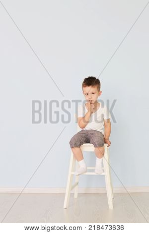 European teenage boy in a white shirt and blue shorts sitting on a chair. Looking at the camera. Studio shot, isolated on white background.