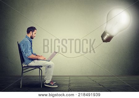 Young professional man using a laptop with light bulb plugged in it isolated on gray wall background