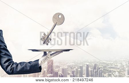 Closeup of waiter's hand in white glove presenting stone key symbol on metal tray with cityscape view on background. 3D rendering.