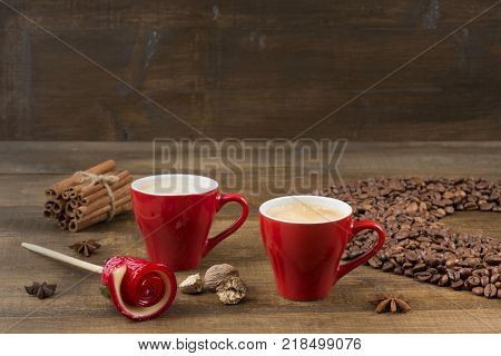 Two cups of coffee with a foam top view. Coffee beans badon cinnamon and caramel on a wooden surface with place for text. Love of a coffee drink. Morning invigorating coffee for two with copy space.
