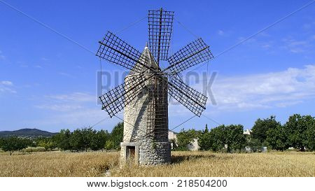 Typical mallorquin windmill on a wheat on the Spanish island in the Mediterranean island of Majorca and green trees against a blue sky
