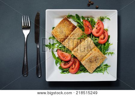 Salad of fried tofu with tomatoes and rocula. Homemade vegetarian salad in a white plate on a black background. A healthy Asian diet vegan vegetarian salad.