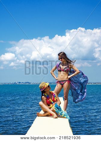 Two beautiful women, has haired long hair, red bikini, poreo, sunglasses, slim body, happy smile face. Tropical hot sea.