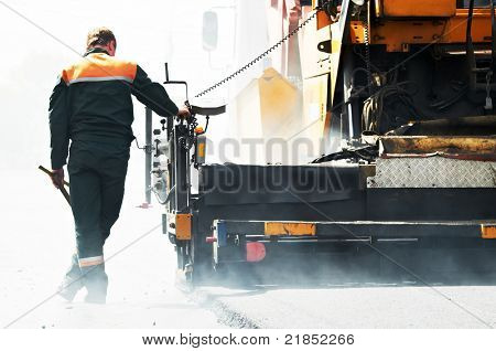 Trabajador operando la máquina pavimentadora de asfalto durante la construcción de carreteras y obras de reparación